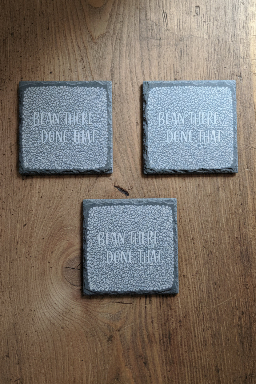 Three square gray stone coasters with a textured border and the words 'BEAN THERE. DONE THAT.